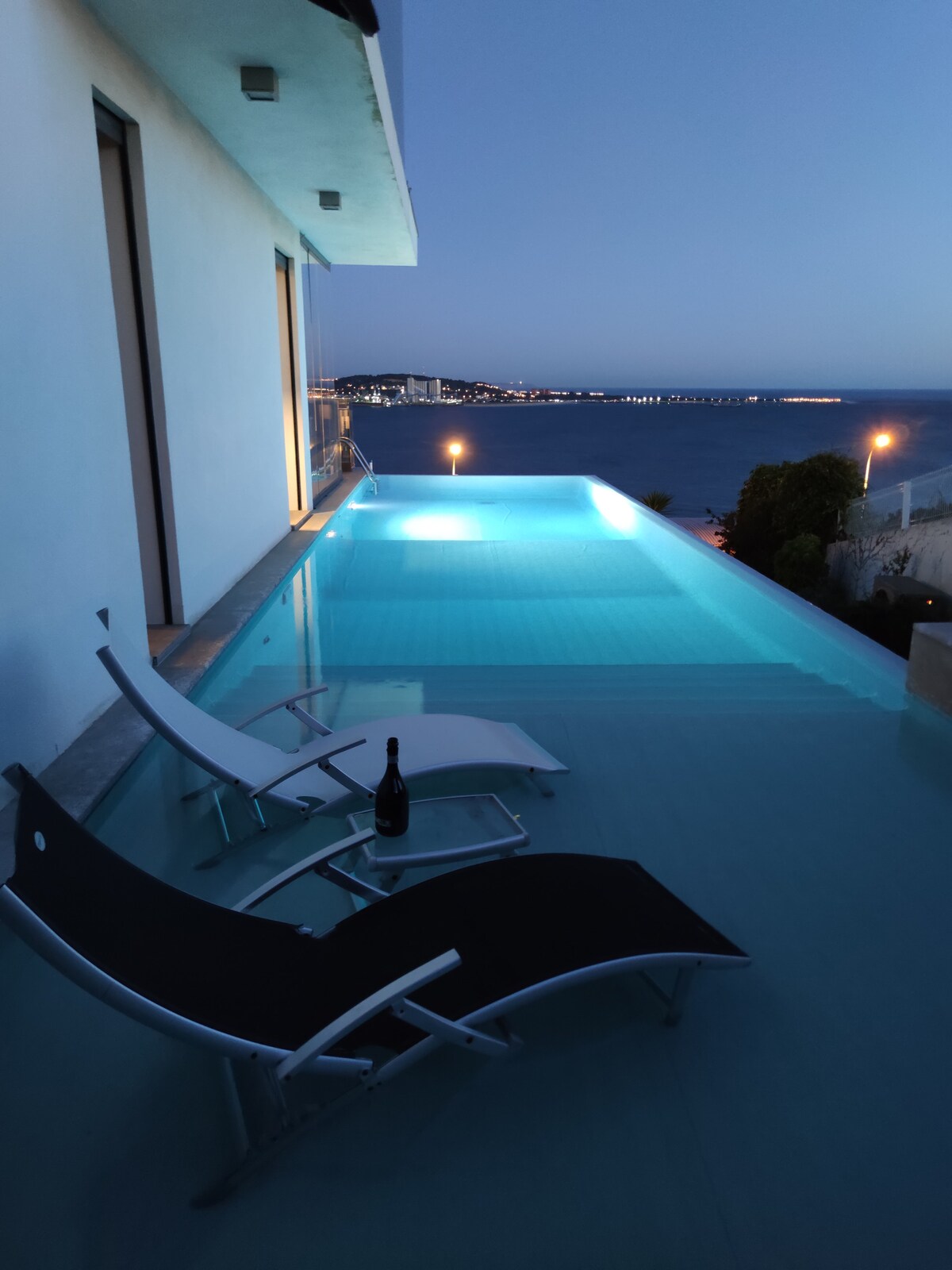 Piscina iluminada ao anoitecer com vista para a costa